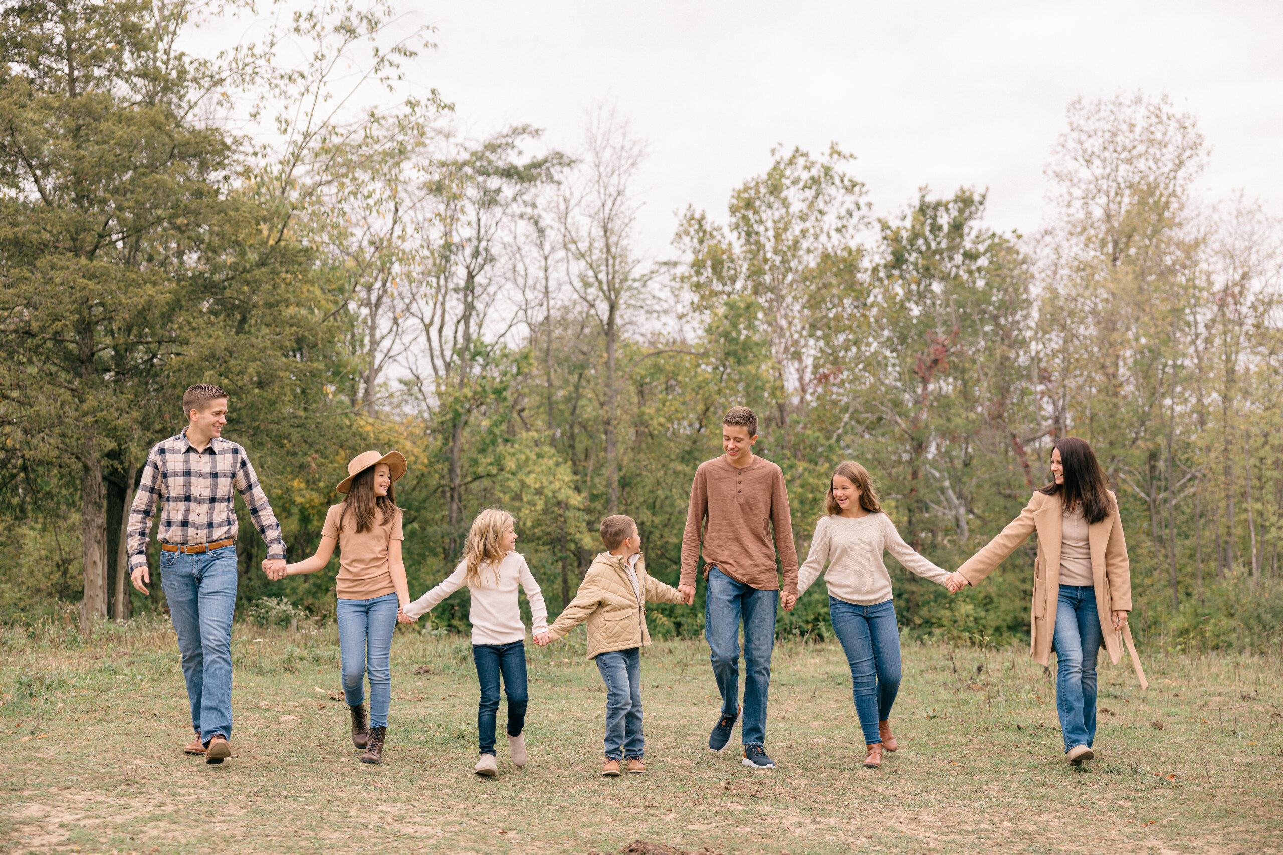 Family of 7 walking hand in hand during their fall family photos in Indianapolis wearing blue jeans and tans and creams