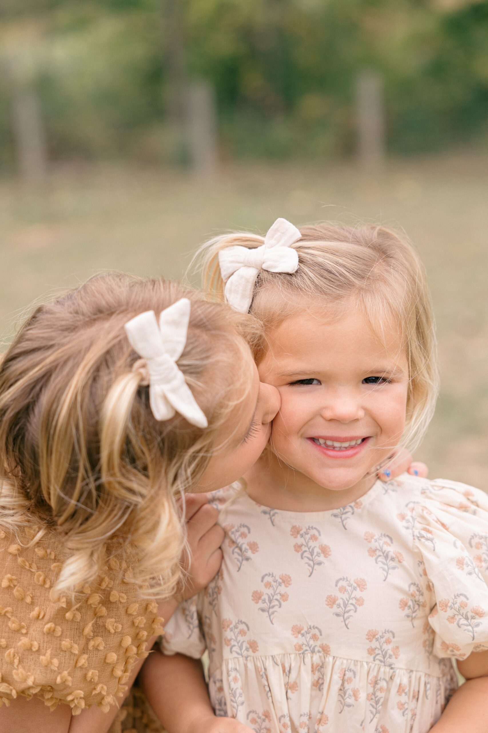 older sister in a tan dress kisses her younger sister's cheek during their fall family photos in Indianapolis