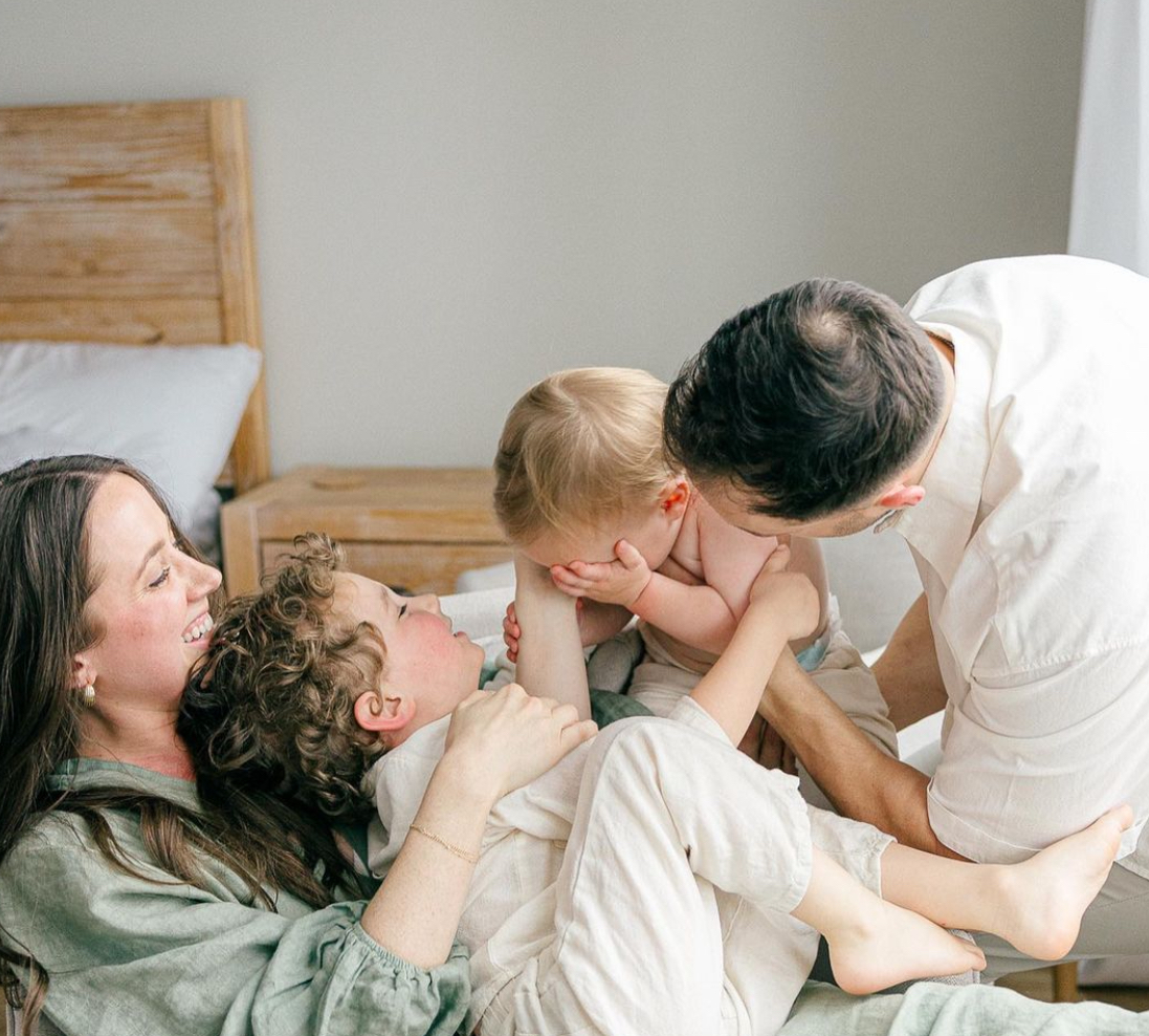 mom in green dress reclines with her young son laying on her lap as dad holds their toddler close to the older boy for tickles, easy photo session with kids