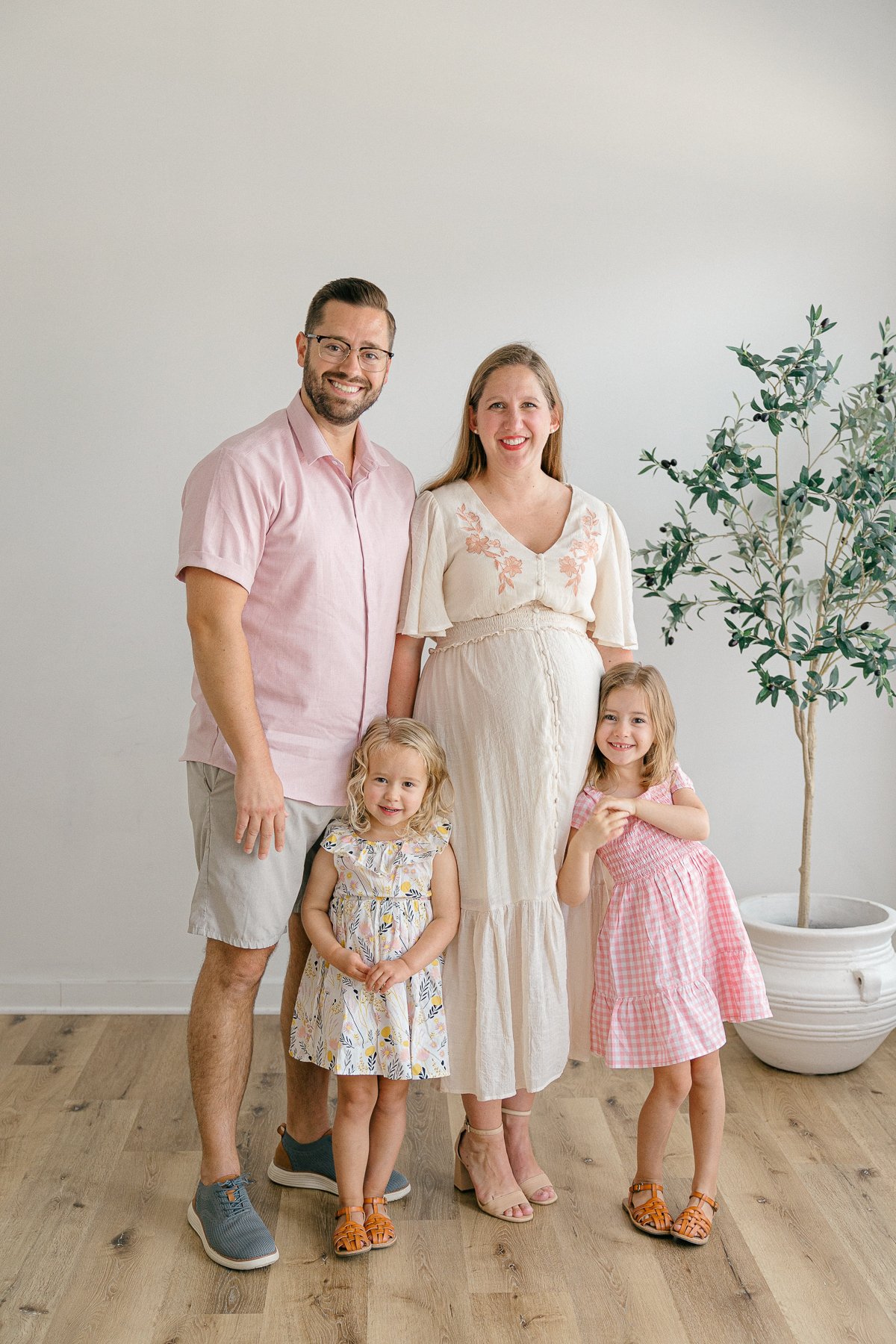 A family of 4 dressed in creams and pinks stand together and smile for a family portrait in Indianapolis