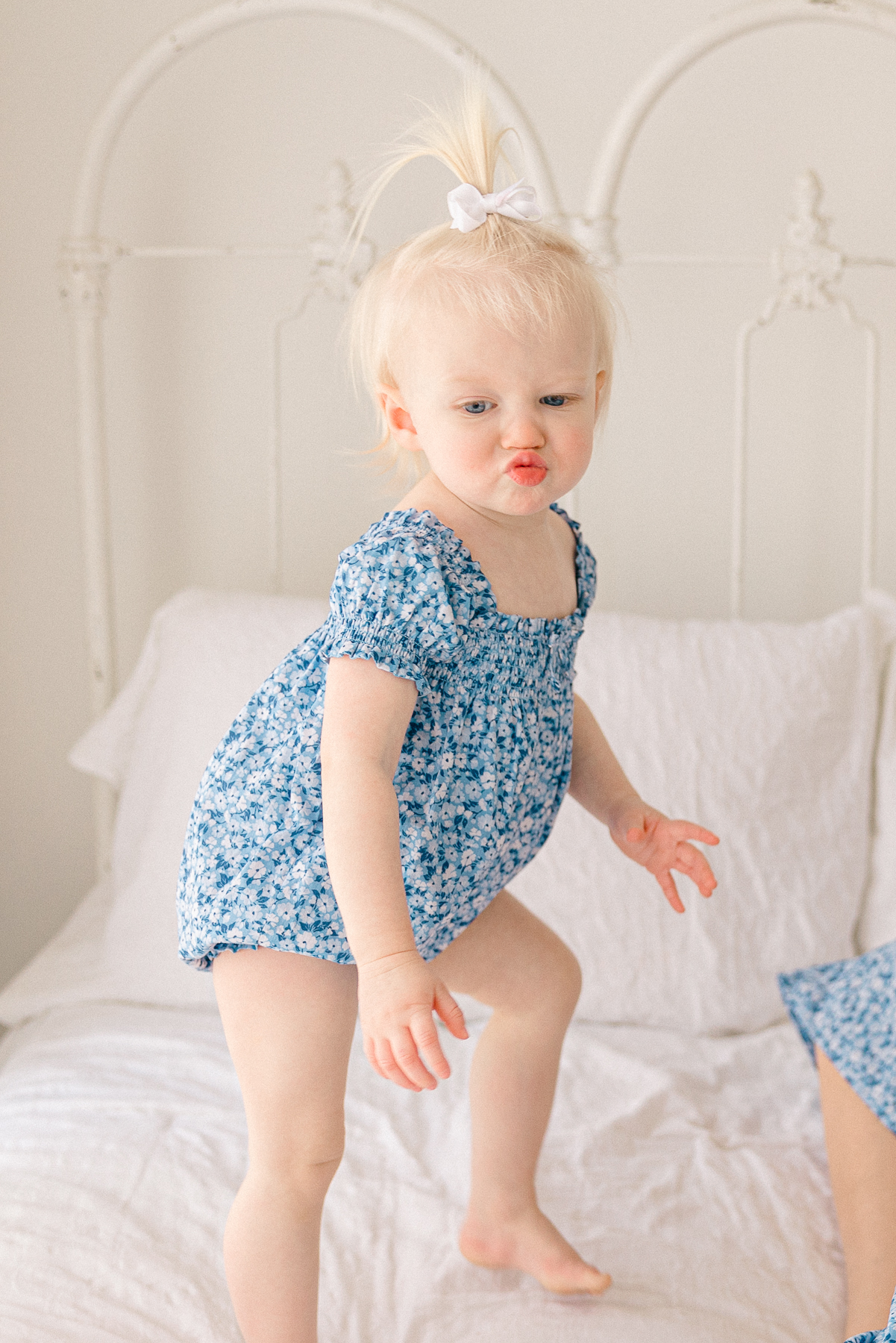 toddler girl in blue floral romper makes a silly face while jumping on the bed, easy photo sessions with kids