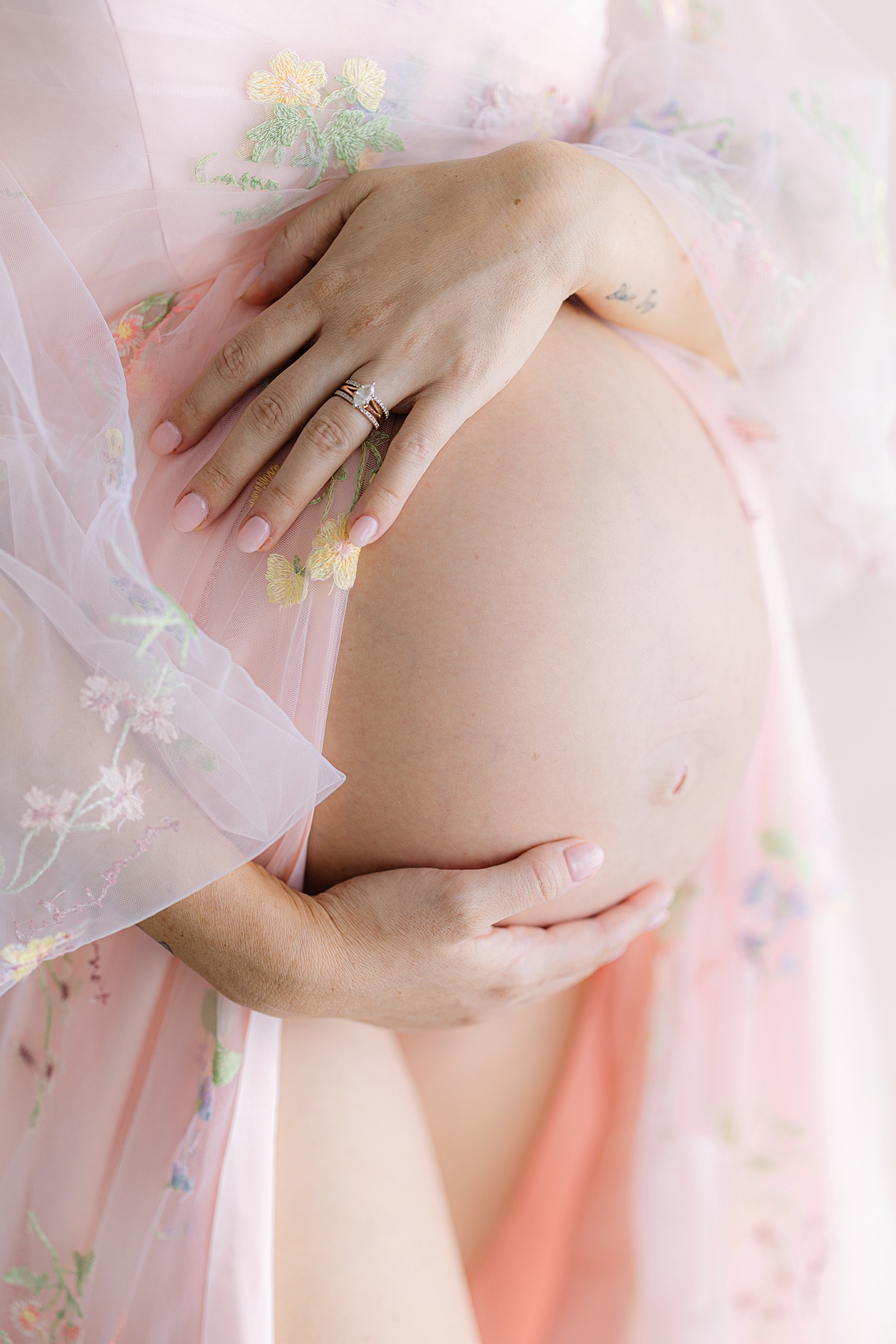 pregnant mother in pink floral dress holds her bare baby bump Indianapolis baby shower venues