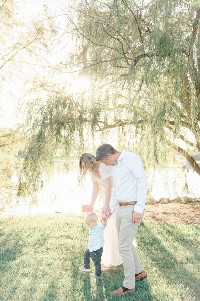 Young family holds hands while walking under a willow tree for their Indianapolis spring family pictures