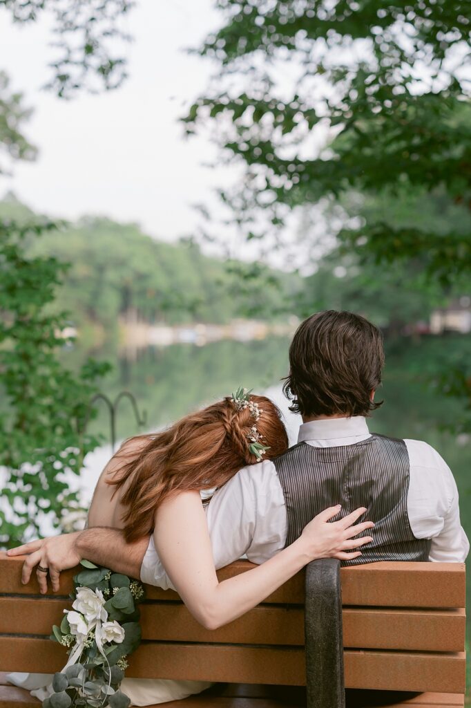 Bride rests her head on her grooms shoulder while sitting on a bench over looking a lake, Indiana wedding photographer 