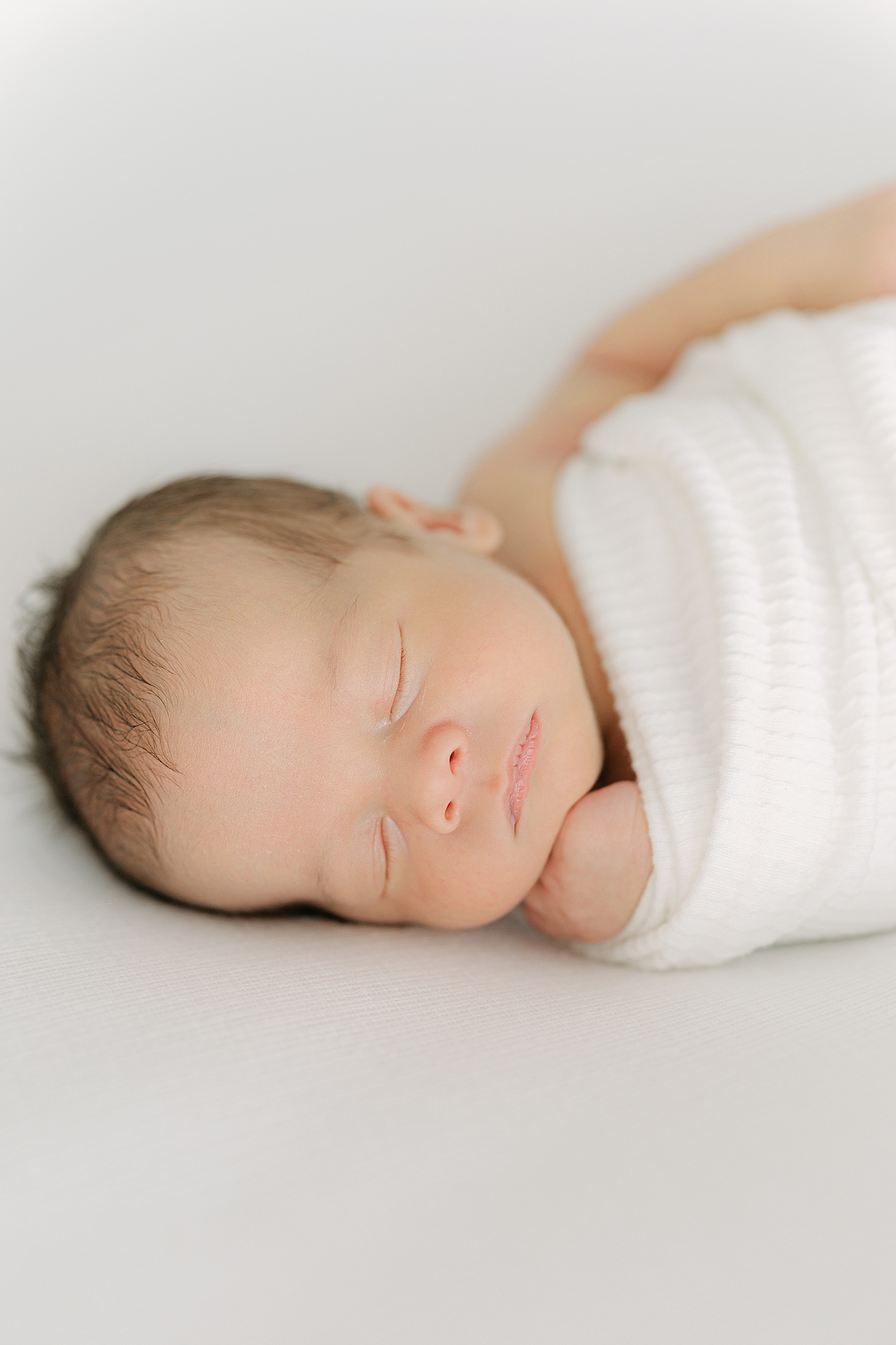 baby swaddled in white blanket sleeps with his fist under his chin during his Indianapolis newborn session