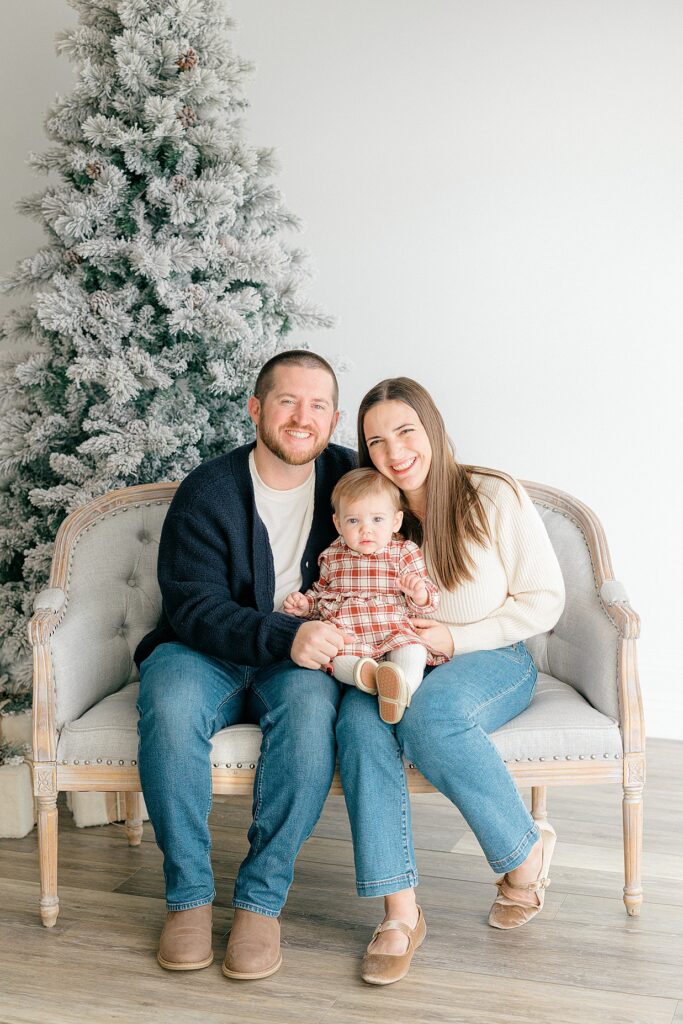 A family of three sits in front of a flocked tree during their Indianapolis Christmas photo session