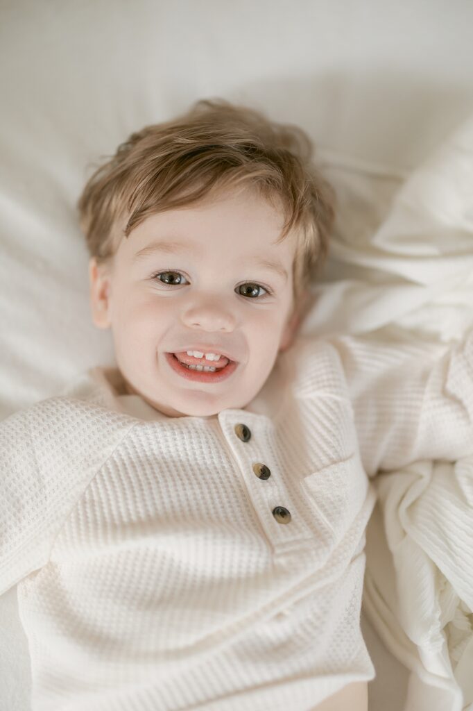 Toddler boy in cream shirt smiles and rolls on the floor mommy and me classes in Indianapolis